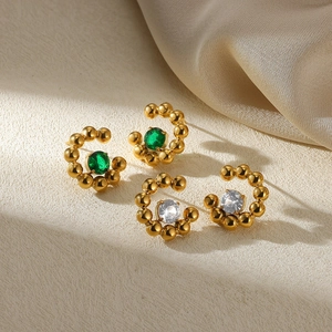 Detail of C-shaped gold beaded earrings featuring emerald green and clear zircon stones