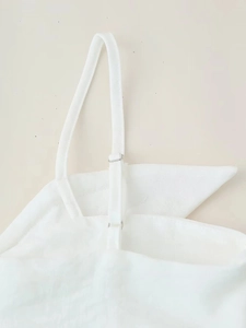 Détail d'une fine bandoulière réglable avec boucle en métal argenté sur une robe blanche