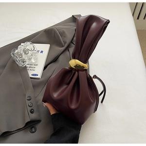 Detail of burgundy drawstring bucket bag featuring a decorative gold irregular metal ring handle