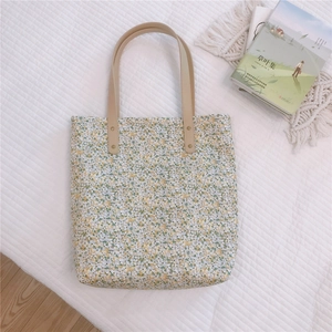 Detail of floral tote bag showing yellow pattern, leather handle, and gold rivet fasteners