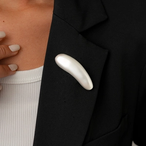 Detail view of a pearl white curved brooch pinned on a professional black blazer lapel