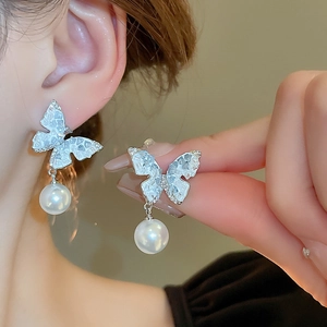 Detailed view of silver butterfly stud earrings with blue stones and white pearls on ear
