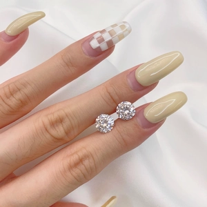 Close-up of sparkling round-cut zircon earrings held by hand on white silk fabric