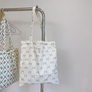 Detail of canvas tote bag with light blue bow print and sewn fabric label on front