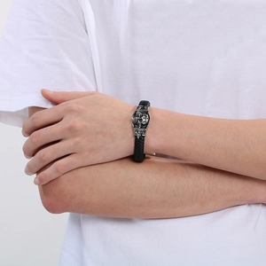 Close-up of a men's black braided leather bracelet with a silver skull charm on wrist