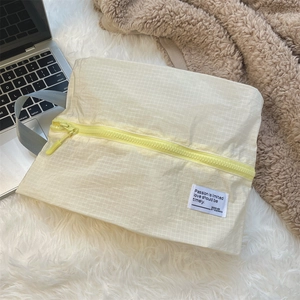 Macro detail of a pale yellow checkered mesh packing cube with zipper and woven handle