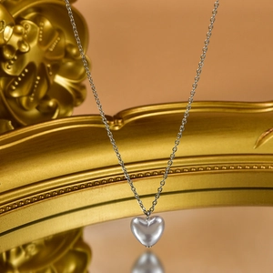 Detail of silver heart pendant with pearl finish hanging on a vintage gold mirror frame