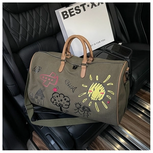 Detail of army green travel bag on car seat featuring colorful doodle patterns and leather straps