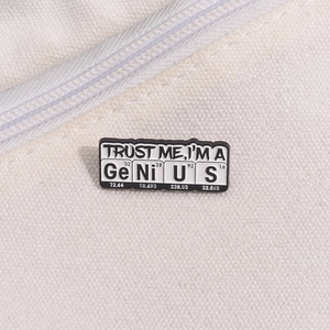 Detail of metal science pin with black enamel finish featuring the word GeNiUS in elements