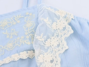 Close-up detail of light blue fabric with white floral embroidery and delicate lace trim