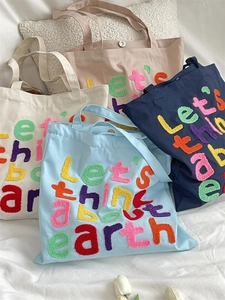 Detail of four colorful canvas tote bags with 'Let's think about earth' chenille embroidery