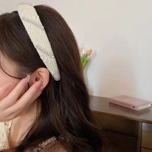 Detail of cream white pleated fabric headband with pearl and chain accents worn by a model