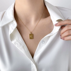 Golden sunburst rectangular pendant necklace on a model wearing a white silk blouse