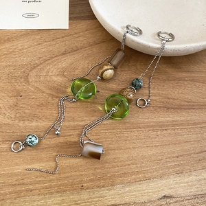 Detailed shot of asymmetrical drop earrings with green beads and silver chains