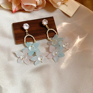 Macro view of floral drop earrings with blue and pink petals on champagne silk background