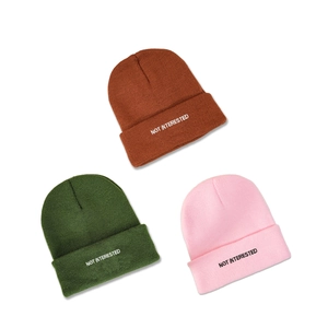 Three minimalist NOT INTERESTED embroidered beanies in brown, dark green, and pink colors