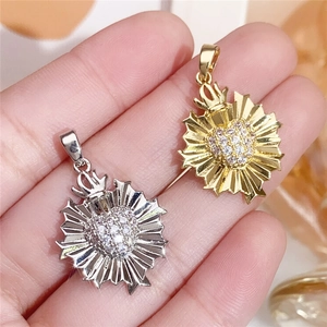 Detail of heart sunburst pendants in gold and silver with zircon inlays held by hand