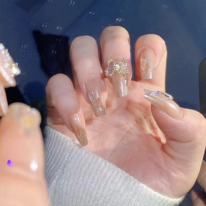 Detailed view of nude gradient press-on nails with 3D crystal bows and glitter accents