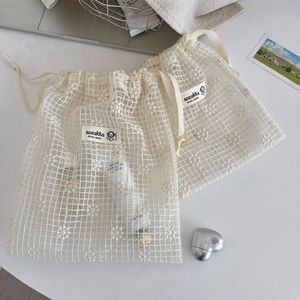 Detail of embroidered daisy mesh storage bag with drawstring on a desk setup