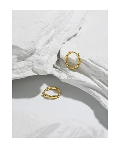 Macro detail of golden irregular twisted hoop earrings on a textured stone background