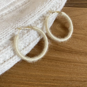 Detail of cream yarn-wrapped hoop earring on textured knit and wooden background