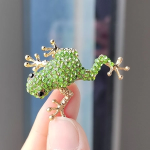 Detailed close-up of a golden frog brooch pavé-set with vibrant green rhinestones