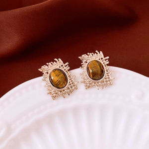 Detailed macro view of vintage oval tiger eye stud earrings on textured ceramic display