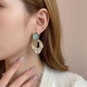 Boucles d'oreilles dorées avec pierre œil-de-chat verte, perles et fleurs sur un mannequin