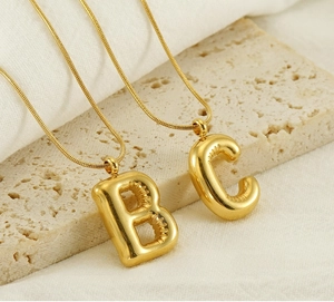 Macro shot of 18k gold plated bubble letter pendants B and C on snake chain
