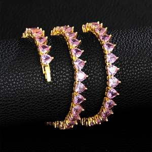 Macro detail of gold tennis chain featuring pink heart zircons on black leather texture