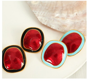 Irregular red gemstone earrings with vintage gold and enamel frames near a sea shell