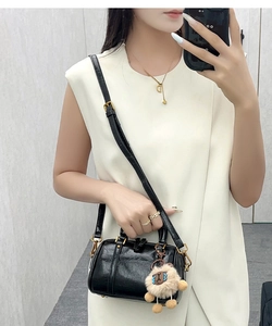 Detail of glossy black leather Boston bag with plush doll charm and long shoulder strap