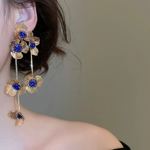 Close-up of elegant gold flower tassel earrings with blue centers on a model