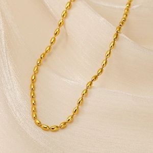 Macro shot of 18K gold plated oval bead chain necklace on beige pleated silk fabric