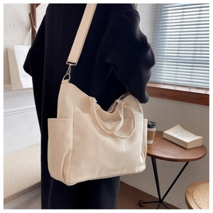 Detail of a large beige canvas tote bag with functional pockets and adjustable strap