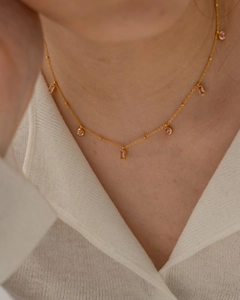 Détail d'un collier en chaîne dorée à billes avec pendentifs en cristal rose et carrés