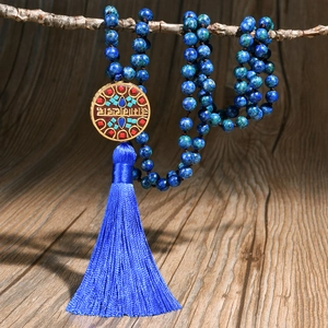 Collana etnica di perline blu con ciondolo dorato e nappa appesa a un ramo di legno