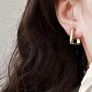 Close-up of a model wearing a golden U-shaped geometric metal earring in a modern style