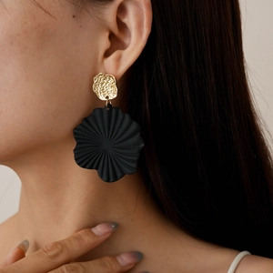 Detail view of a model wearing gold hammered studs and black pleated petal drop earrings