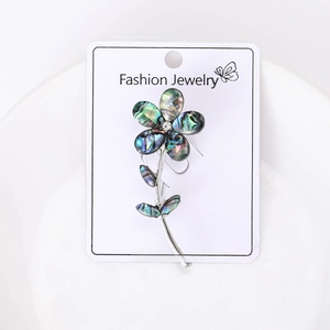 Close-up of abalone shell flower brooch with rhinestone center on white card