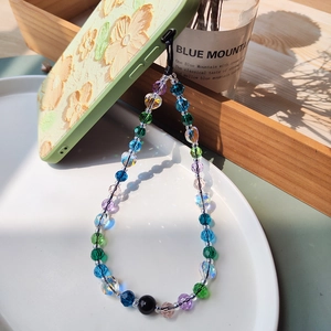 Colorful crystal bead phone strap with heart charm on a white plate and green case