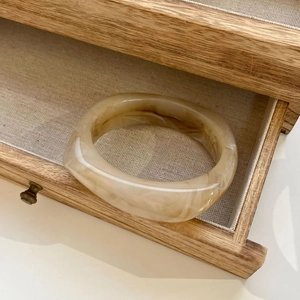 Detailed texture of amber marble resin bangle inside a wooden jewelry drawer