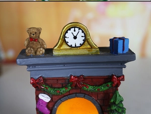 Detailed view of a glowing Christmas resin fireplace with a teddy bear and clock ornament