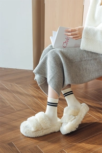 Close-up of beige plush slippers paired with warm black and white striped wool socks