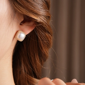 Close-up of a square pearl earring with gold trim and tiny zircon accents on ear