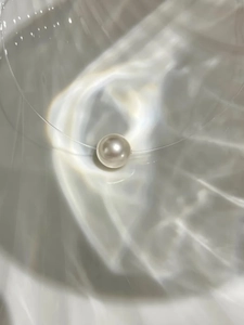 Detailed view of a round pearl pendant on a minimalist invisible string necklace
