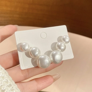 Close-up of V-shaped white pearl earrings with six graduated pearls on a display card