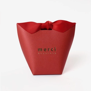 Elegant red gift box with large ribbon bow and gold Merci Beaucoup lettering on white