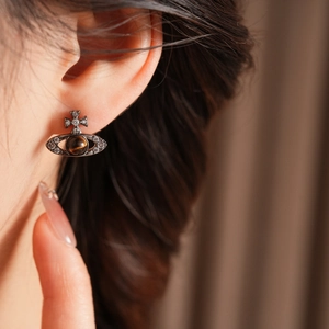 Gros plan d'une boucle d'oreille Saturne avec pierre œil de tigre marron et zircons