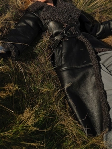 Detail of long shearling coat featuring black leather and grey faux fur trim with belt